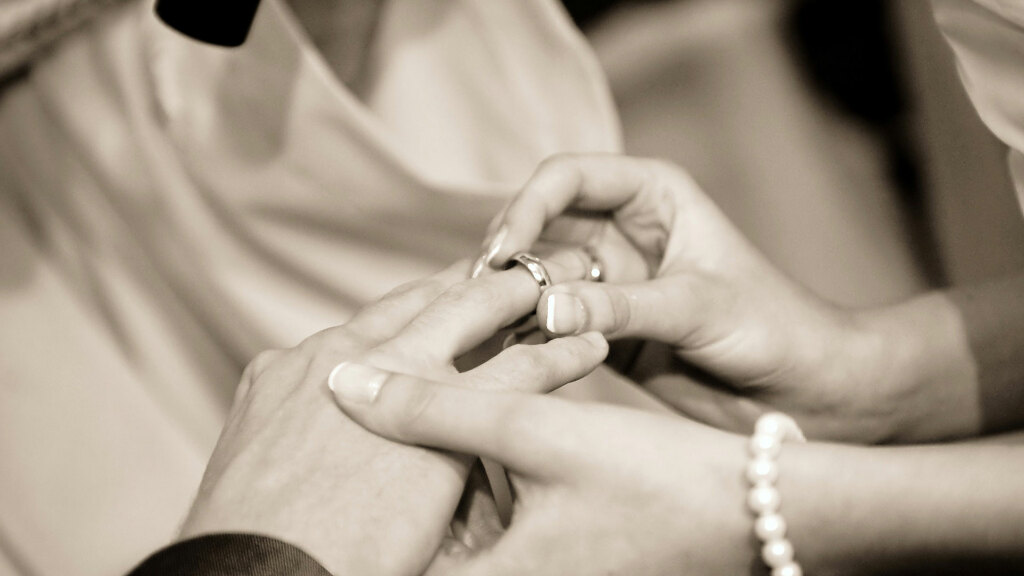Sie sehen, wie während einer Hochzeit die Ringe angesteckt werden.