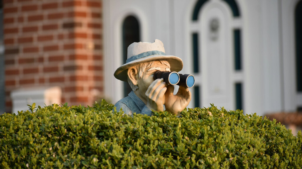 Sie sehen eine Figur, die einen Mann darstellt, der mit einem Fernglas in der Hecke sitzt.