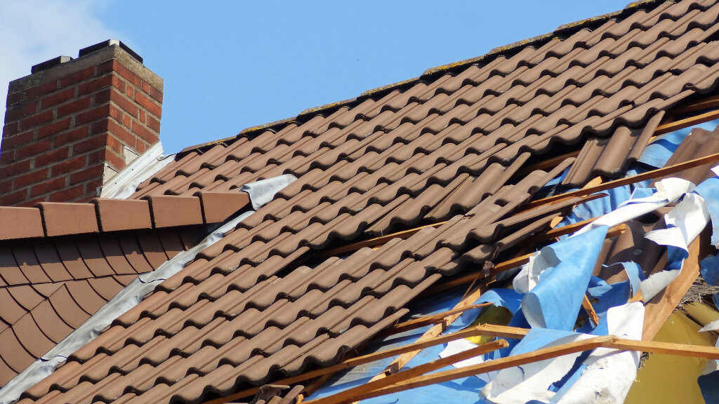 Sie sehen einen Teil eines Daches, welches durch einen Sturm stark beschädigt wurde.