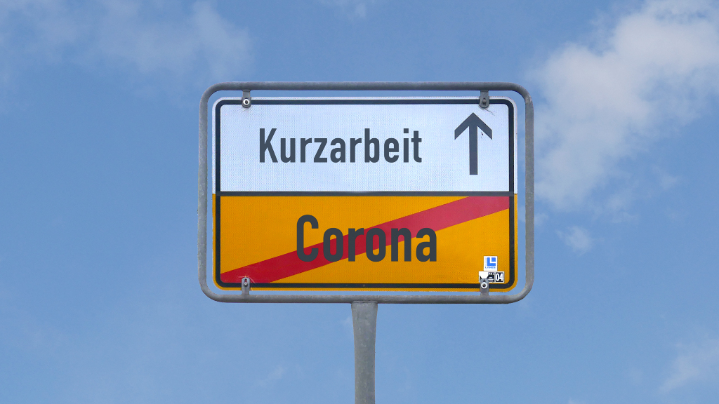 Sie sehen die Rückseite eines Ortschilds, welches symbolisiert, dass die „Corona“-Pandemie (COVID-19) viele Menschen in die „Kurzarbeit“ geführt hat, um vorerst dem Arbeitsplatzverlust vorzubeugen.