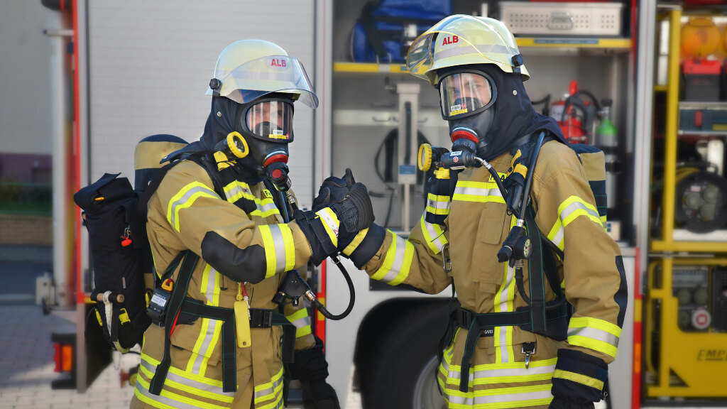 Sie sehen zwei Feuerwehrmänner mit Atemschutzmasken.