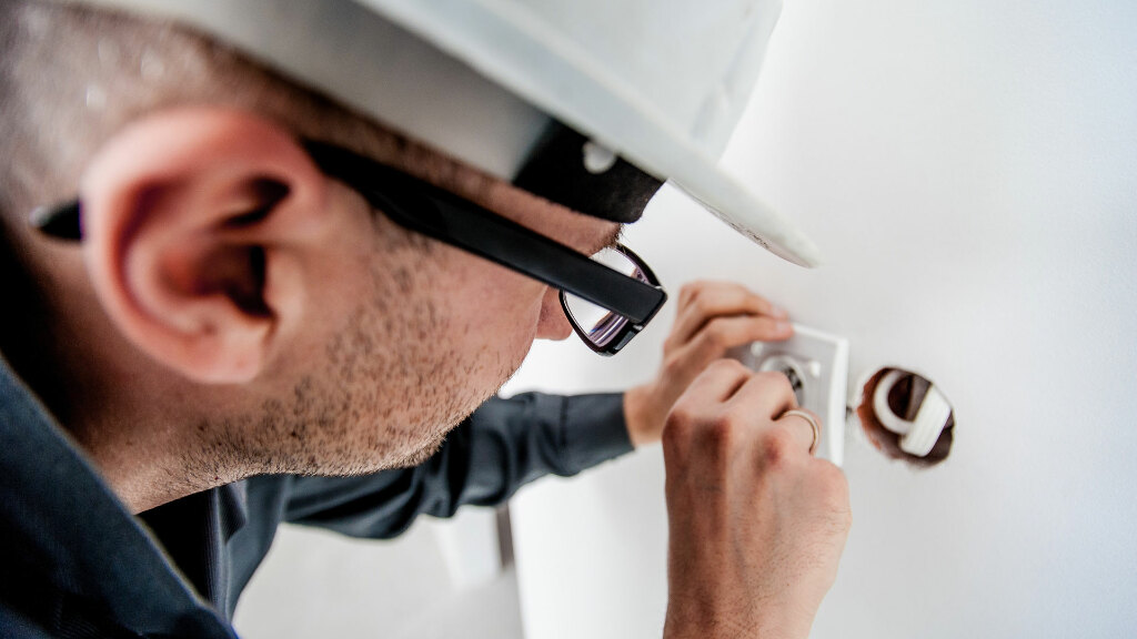 Sie sehen einen Elektriker, der eine Steckdose in eine Wand einbaut.