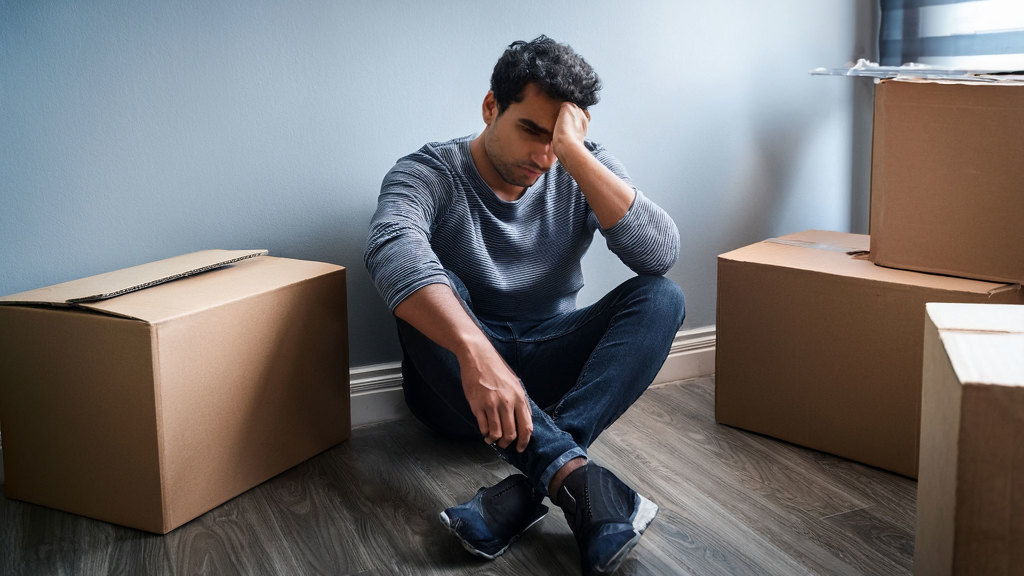 Sie sehen einen traurigen (verzweifelten) Mann, der in einem leeren Zimmer mit Umzugskartons sitzt.