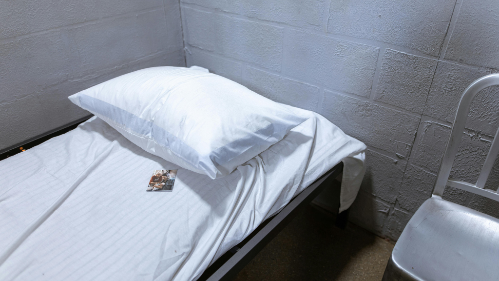 Sie sehen ein Bett in einer Gefängniszelle, auf dem ein persönliches Bild liegt.