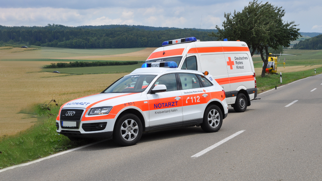 Sie sehen einen Notarzt- und einen Rettungswagen am Straßenrand stehen.