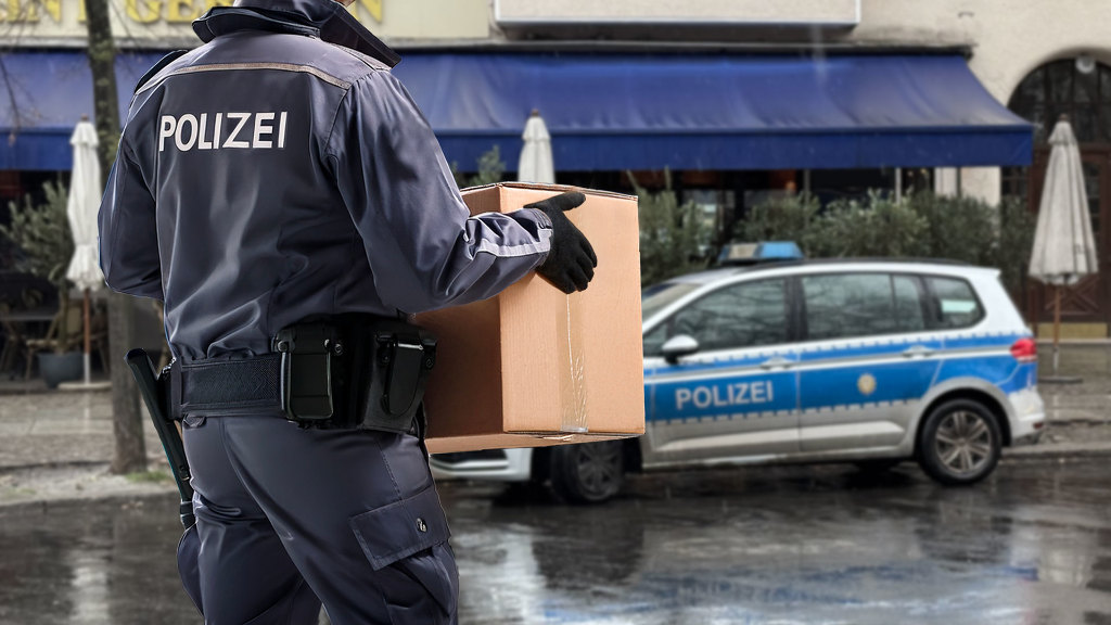 Sie sehen einen Polizisten, der eine Umzugskiste zu seinem Streifenwagen trägt.