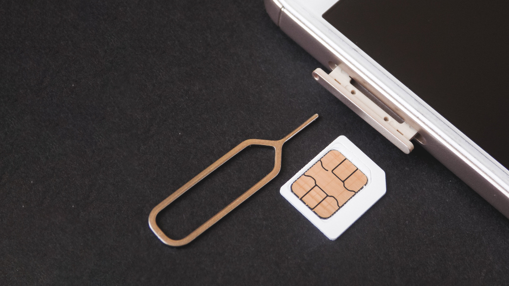 Sie sehen eine SIM-Karte neben einem Smartphone mit offenem Einschub für die SIM-Karte.