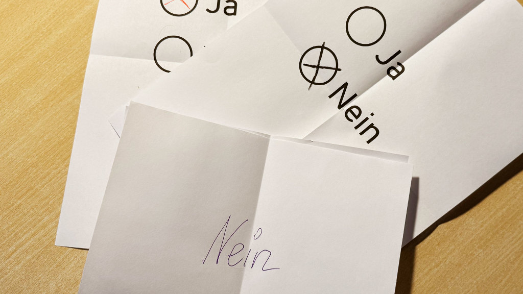 Sie sehen mehrere Stimmzettel mit einem Kreuz für „ja“ bzw. „nein“ und einen teilweise zugeklappten Stimmzettel mit dem Wort „nein“.