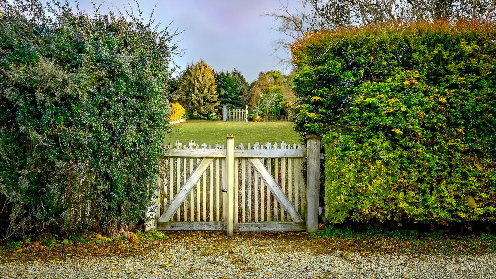 Sie sehen einen Zaun mit Tor, umringt von einer Hecke, der den Zugang zu einem Grundstück versperrt.