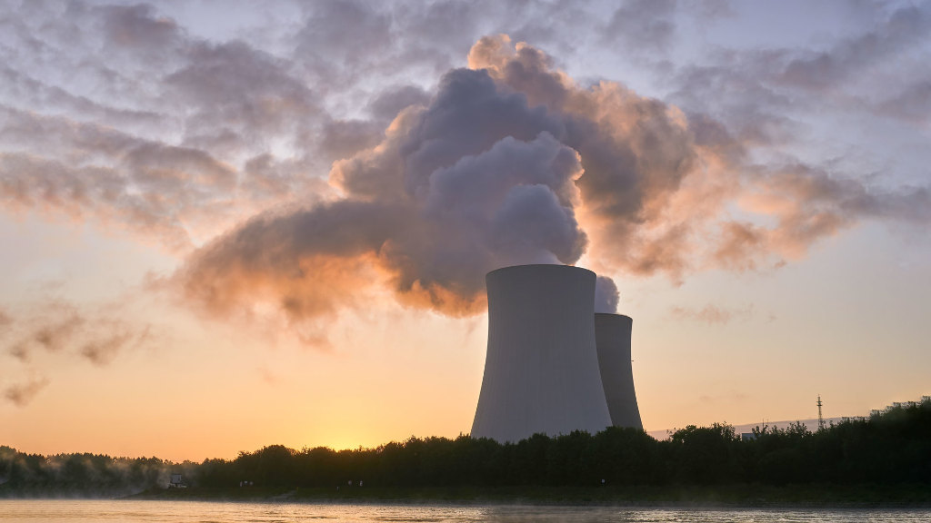 Sie sehen die Kühltürme eines Kernkraftwerks an einem Fluss.