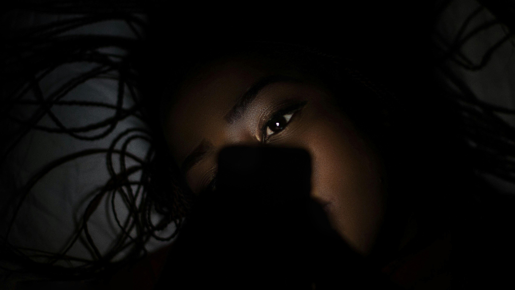 Sie sehen ein trauriges Mädchen in der Duneklheit, davor ein Handy.