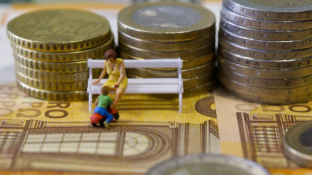 Sie sehen eine Frau und ein Kind auf einer Bank, die auf Euro-Banknoten und vor Münzstapeln steht.
