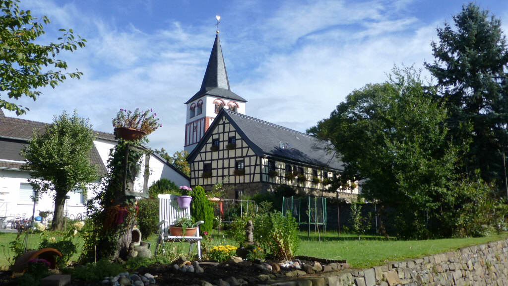 Sie sehen die Pfarrkirche St. Pankratius und davor einen dekorativen Garten.
