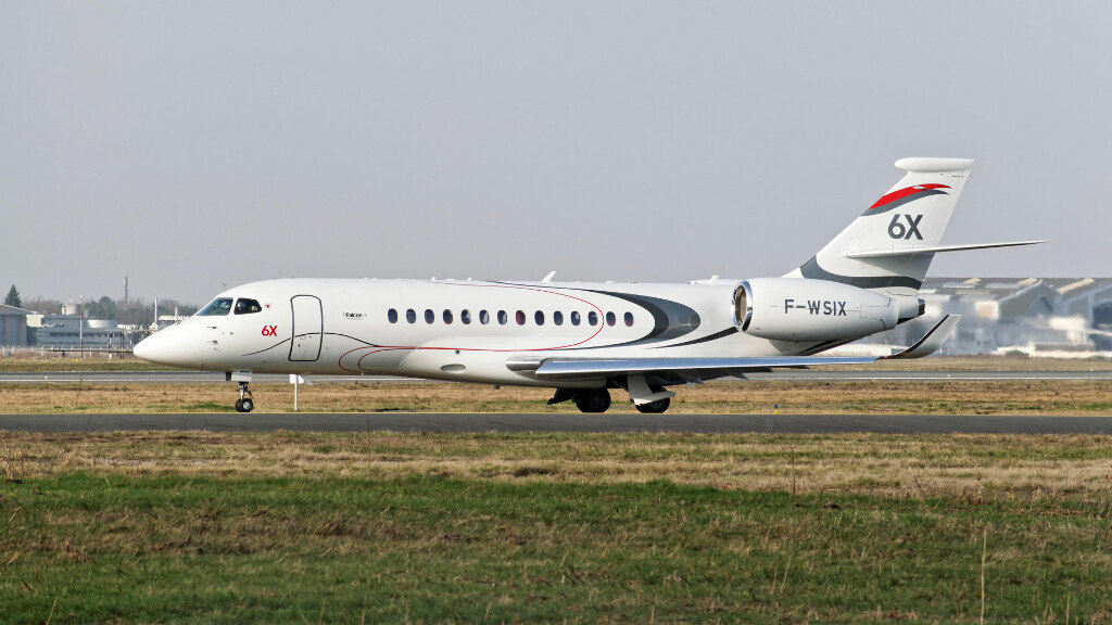 Sie sehen ein Geschäftsflugzeug vom Typ Falcon 6x des Hersteller Dassault Aviation auf der Rollbahn eines Flughafens.