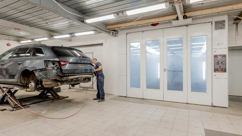 Sie sehen eine Autowerkstatt mit einem teilweise zerlegten, aufgebockten Auto.