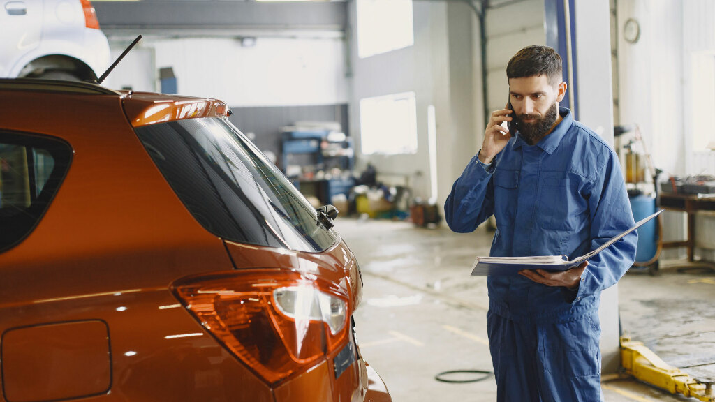 Sie sehen einen Automechaniker, der telefoniert und dabei ein Auto ansieht.