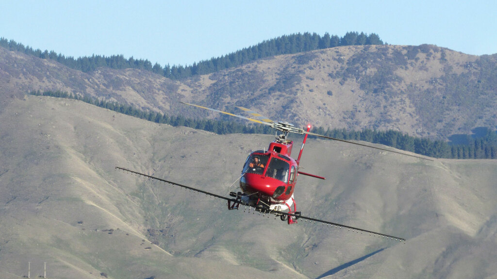 Sie sehen einen Hubschrauber zum Versprühen von Pflanzenschutzmitteln im Flug.