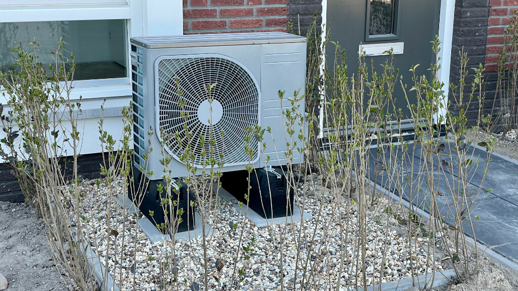 Sie sehen die Außeneinheit einer Wärmepumpe vor einem Gebäude.
