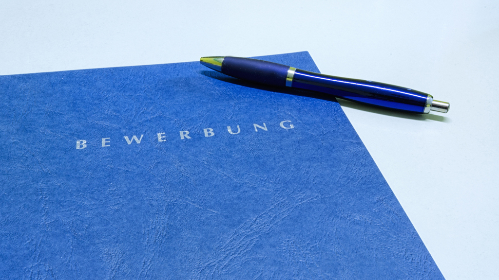 Sie sehen eine blaue Bewerbungsmappe und einen blauen Kugelschreiber.