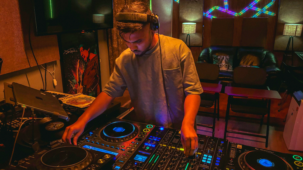 Sie sehen einen DJ, der Live-Musik in einem lebendigen Studio mit Neonlichtern und professioneller Ausrüstung spielt.