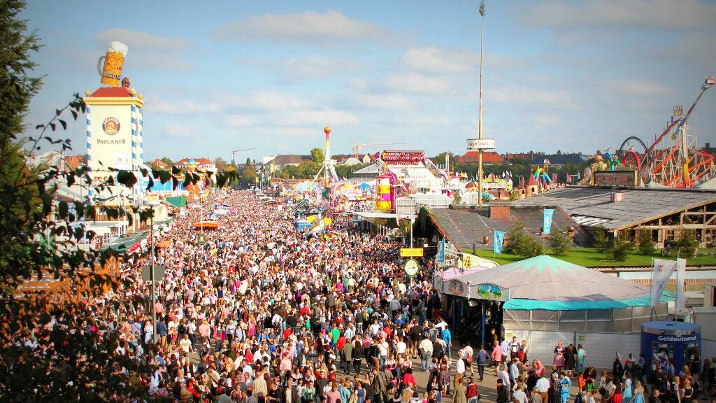 Sie sehen eine lebhafte Szene auf dem Oktoberfest in München, mit vielen Menschen, welche die Festlichkeiten und Attraktionen genießen.