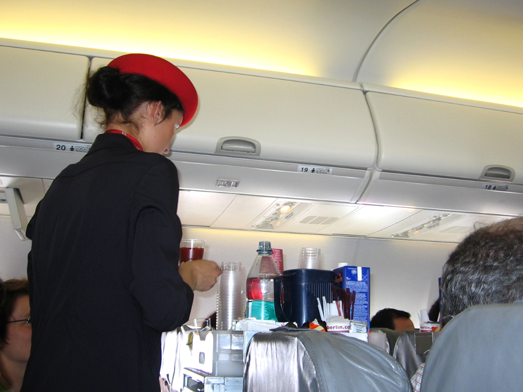 Sie sehen eine Flugbegleiterin beim Verteilen von Getränken und Snacks im Flugzeug.