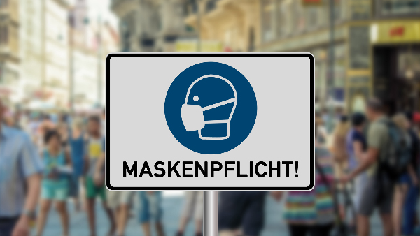 Sie sehen eine eigt ein gezeichnetes Warnschild zum Einhalten der allgemeinen Maskenpflicht.