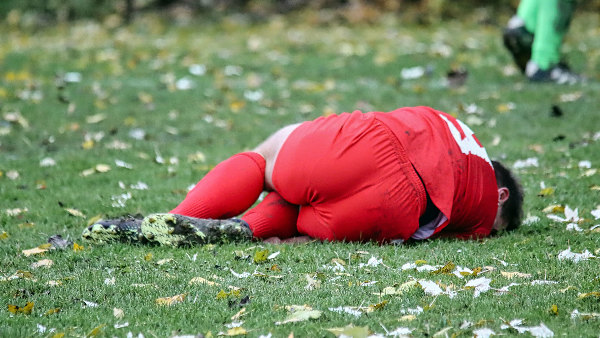 Sie sehen einen Fußballspieler, der mit offensichtlichen Schmerzen auf dem Rasen liegt.