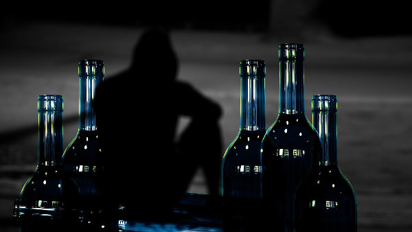 Sie sehen leere Flaschen mit einen schwarzen Schatten einer Person im Hintergrund.