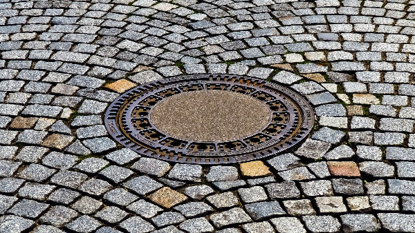 Sie sehen ein Kopfsteinpflaster mit einem eingelassenen Gullideckel.