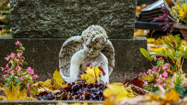 Sie sehen eine kleine Engelsfigur als Grabschmuck auf einem Friedhof.