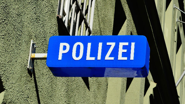 Sie sehen das Schild einer Polizeiwache an einer Hauswand.