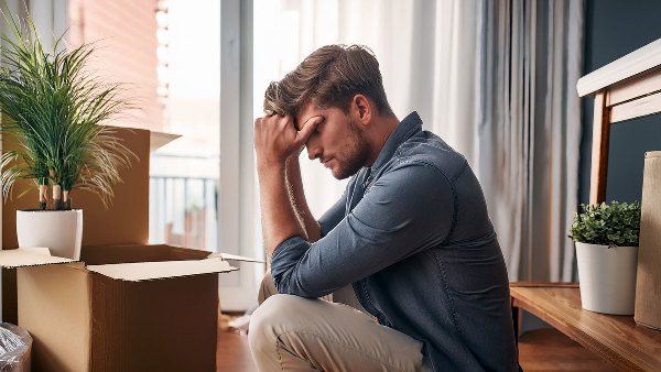 Sie sehen einen traurigen (verzweifelten) Mann, der in einem leeren Zimmer mit Umzugskartons sitzt.