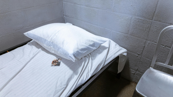 Sie sehen ein Bett in einer Gefängniszelle, auf dem ein persönliches Bild liegt.