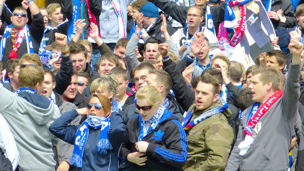 Sie sehen eine Gruppe von Fußballfans beim Jubeln.