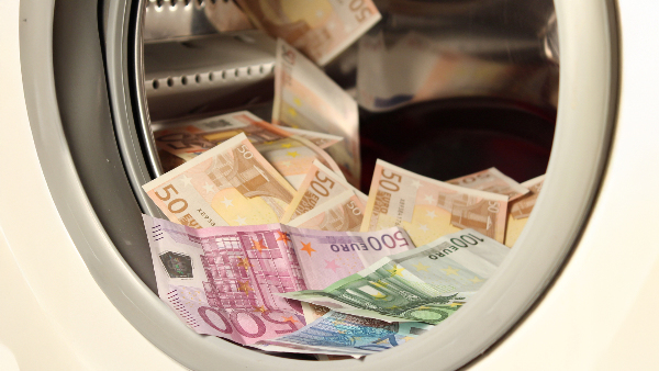 Sie sehen verschiedene Euro-Geldscheine in einer offenen Trommel einer Waschmaschine liegen.