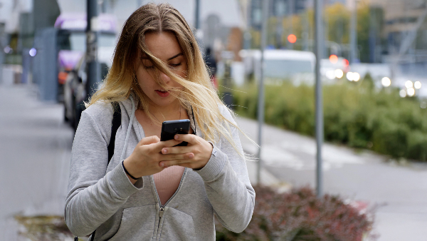 Sie sehen eine junge Frau die eilig ihr Smartphone bedient.