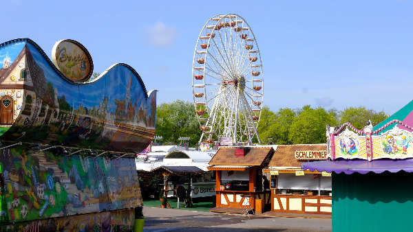 Sie sehen ein Riesenrad und verschiedene Buden auf einem Rummel oder Festplatz.