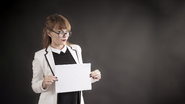 Sie sehen eine junge Frau, die ein weißes Blatt vor sich hält.