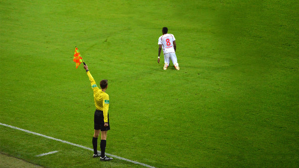 Sie sehen einen knieenden Fußballspieler und einen Schiedsrichter, der eine Strafe anzeigt, auf dem Rasen.