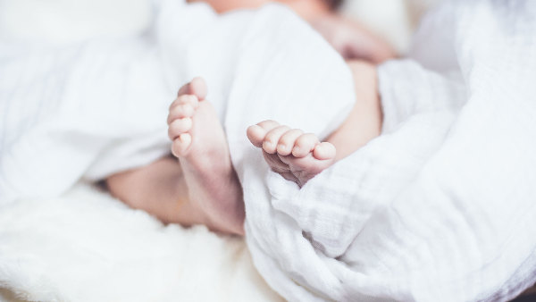Sie sehen die Füsse eines Babys eingewickelt in ein Laken.