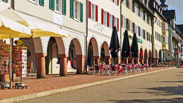 Sie sehen einen Fußweg in einer Stadt, auf dem Tische und Stühle eines Restaurants stehen.