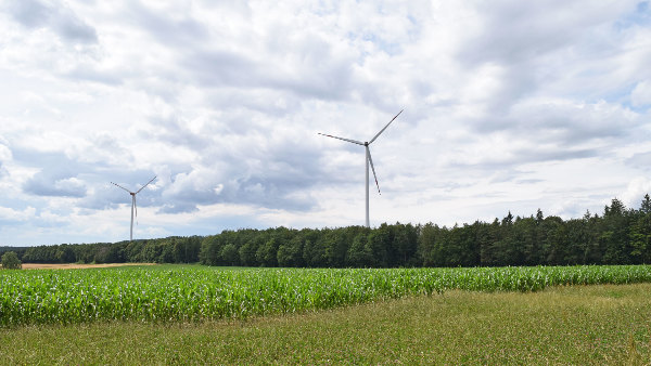 Sie sehen zwei Windkraftwerke in einer Feldlandschaft.