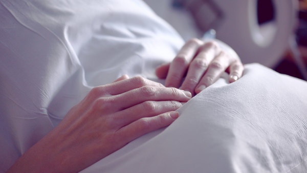 Sie sehen ein Krankenhausbett und die gefalteten Hände einer Person.