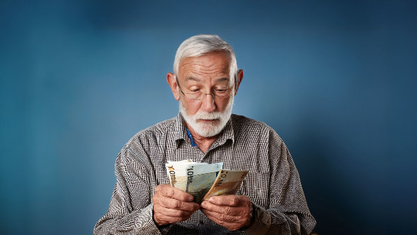 Sie sehen einen alten Mann der ein Bündel Geld in der Hand hat.