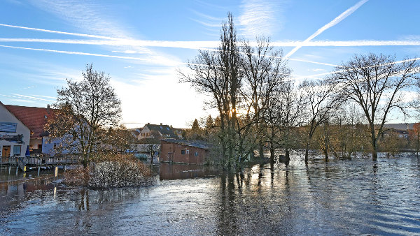 Sie sehen ein überflutetes Flussufer mit betroffenen Gebäuden.