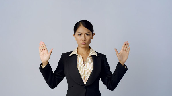 Sie sehen eine Frau in Businesskleidung, welche die Hände abwehrend erhoben hält.