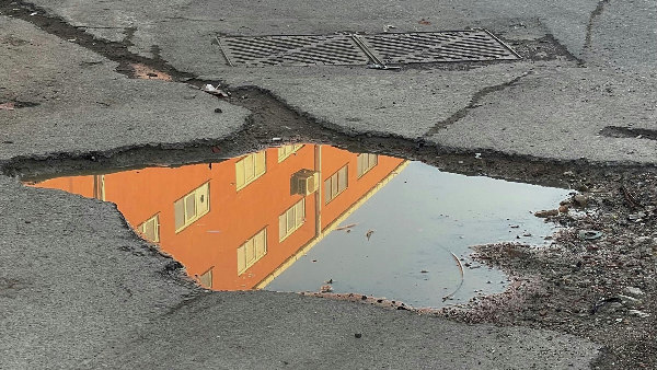 Sie sehen ein Schlagloch in dem sich ein Haus spiegelt.