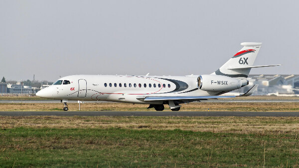 Sie sehen ein Geschäftsflugzeug vom Typ Falcon 6x des Hersteller Dassault Aviation auf der Rollbahn eines Flughafens.