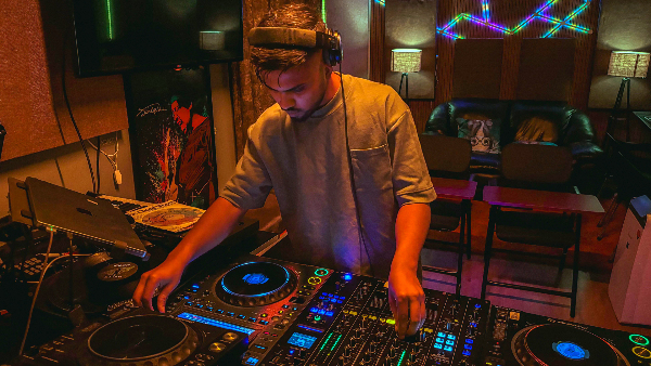 Sie sehen einen DJ, der Live-Musik in einem lebendigen Studio mit Neonlichtern und professioneller Ausrüstung spielt.